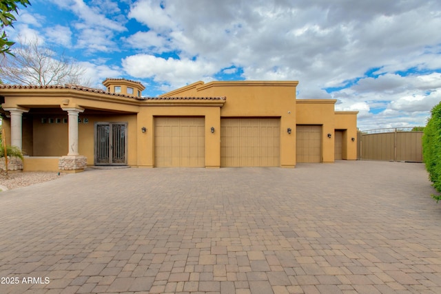 view of front facade with decorative driveway, a gate, an attached garage, and stucco siding