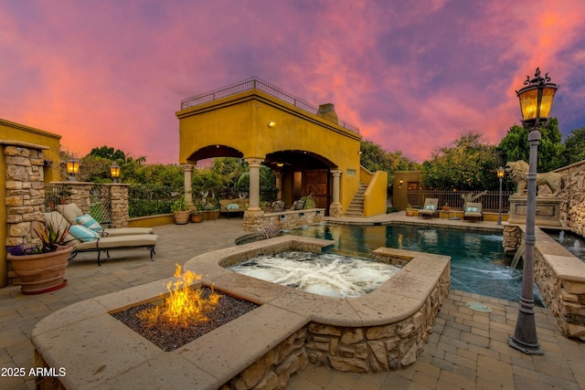 patio terrace at dusk with a fenced in pool, an in ground hot tub, a balcony, and fence