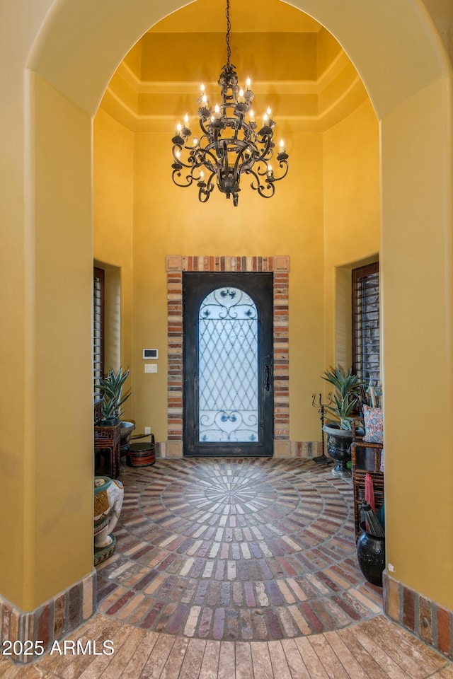 foyer featuring a tray ceiling, arched walkways, a notable chandelier, and a high ceiling