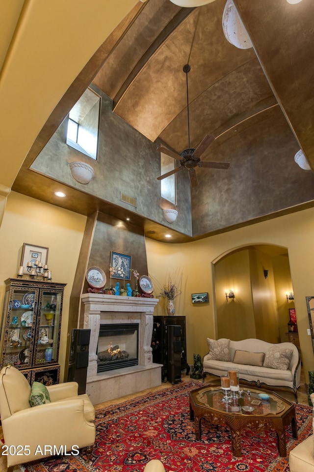 living area featuring arched walkways, a high ceiling, a fireplace, and a ceiling fan