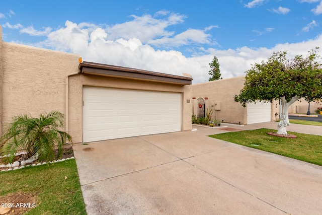 pueblo-style house with driveway, an attached garage, and stucco siding