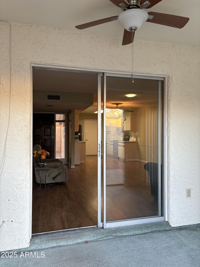 view of exterior entry featuring a ceiling fan, visible vents, and stucco siding