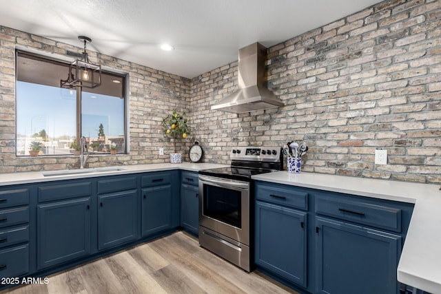 kitchen with light countertops, stainless steel range with electric cooktop, a sink, blue cabinets, and wall chimney exhaust hood