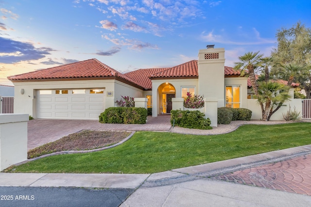 mediterranean / spanish house with an attached garage, a tile roof, decorative driveway, stucco siding, and a chimney