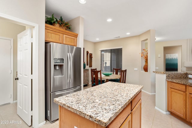 kitchen with light stone countertops, stainless steel fridge with ice dispenser, light tile patterned floors, and a kitchen island