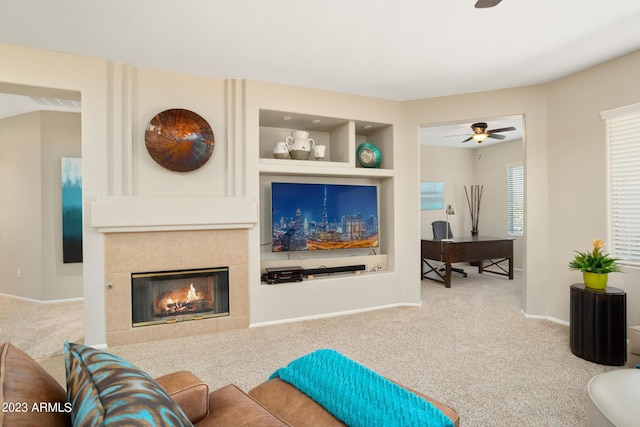 living room with carpet flooring, ceiling fan, built in features, and a tiled fireplace