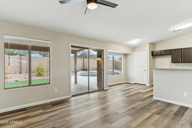unfurnished living room with ceiling fan, baseboards, light wood-style floors, and vaulted ceiling