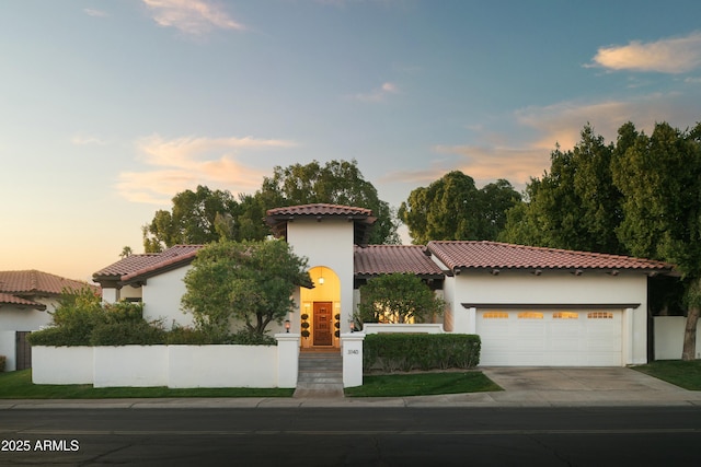 mediterranean / spanish-style house featuring driveway, a garage, a tiled roof, fence, and stucco siding