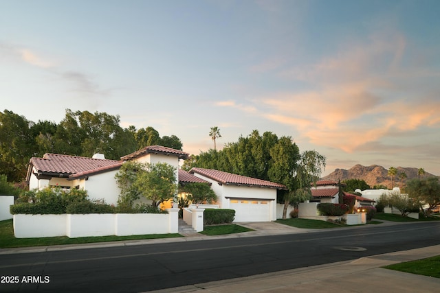 mediterranean / spanish-style house with a tile roof, stucco siding, a mountain view, fence, and driveway