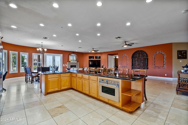 kitchen with a kitchen bar, stainless steel oven, ceiling fan with notable chandelier, a large island with sink, and pendant lighting