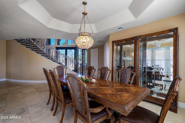 dining area with light tile patterned floors, a raised ceiling, and a notable chandelier