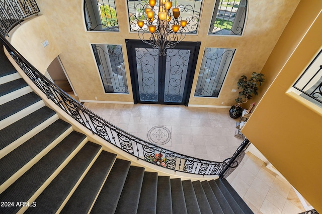 tiled foyer entrance featuring french doors, a towering ceiling, and an inviting chandelier