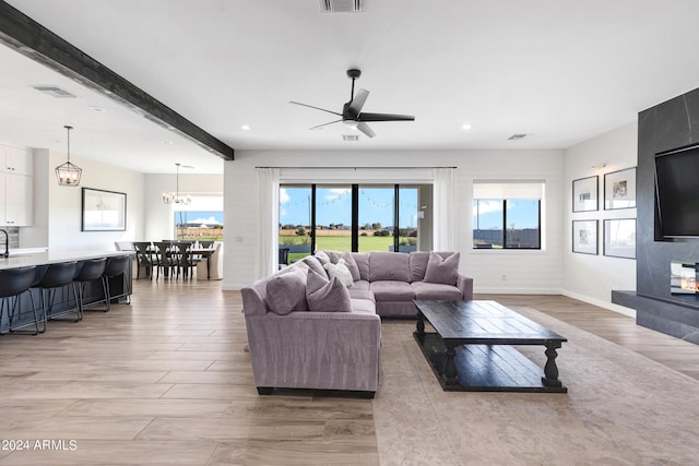 living room featuring beam ceiling, light wood-type flooring, and ceiling fan with notable chandelier