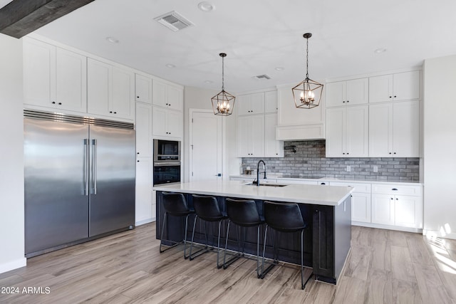 kitchen with stainless steel appliances, light wood-type flooring, a center island with sink, and white cabinets