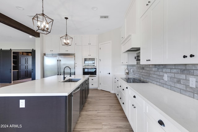 kitchen with a barn door, sink, built in appliances, and an island with sink