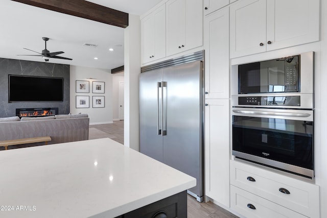 kitchen featuring light hardwood / wood-style flooring, white cabinetry, a large fireplace, and built in appliances