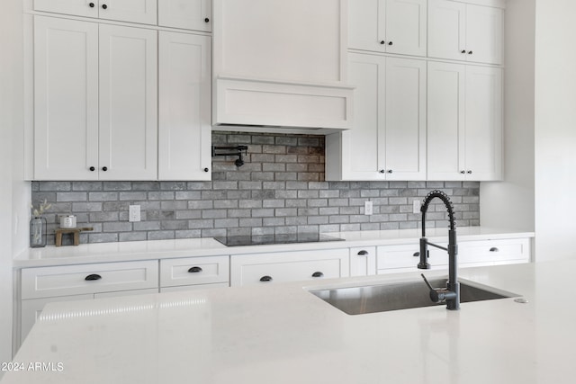 kitchen with black electric stovetop, tasteful backsplash, sink, and white cabinets