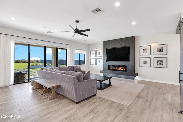 living room featuring a large fireplace, light hardwood / wood-style flooring, and ceiling fan