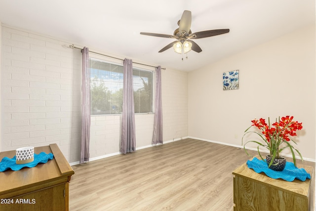 living area featuring hardwood / wood-style flooring, brick wall, and ceiling fan