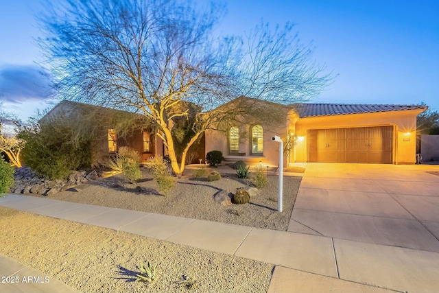 view of front of home featuring a garage, driveway, a tile roof, and stucco siding