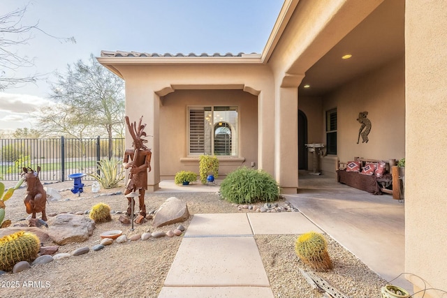 view of exterior entry featuring a patio area, fence, and stucco siding