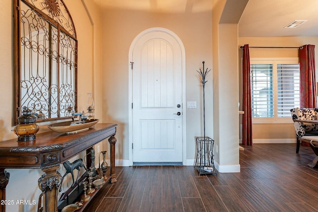 foyer with baseboards, visible vents, arched walkways, and dark wood-style flooring