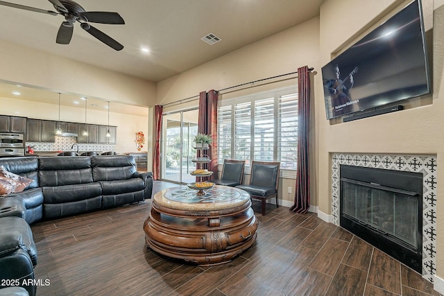 living area featuring wood finish floors, a fireplace, visible vents, ceiling fan, and baseboards