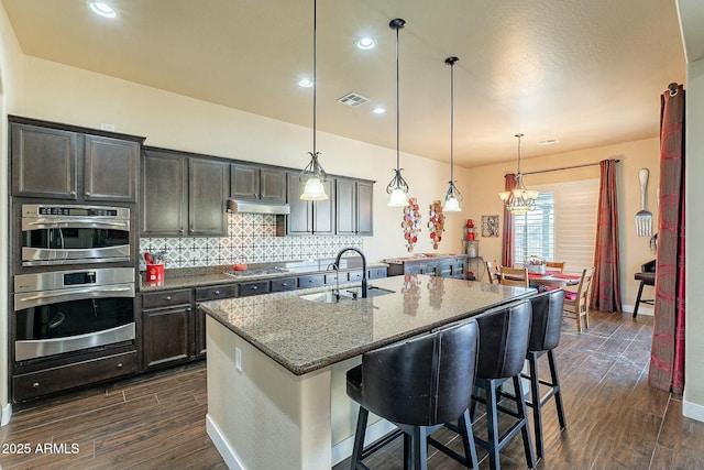 kitchen featuring tasteful backsplash, dark stone counters, dark wood-style flooring, and a sink