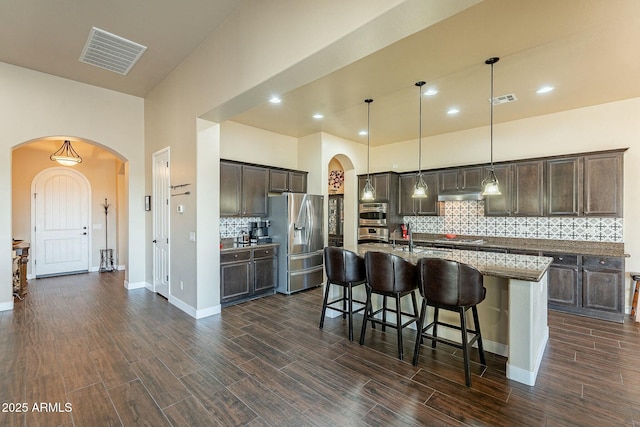 kitchen featuring range hood, a breakfast bar, stainless steel appliances, visible vents, and dark brown cabinetry