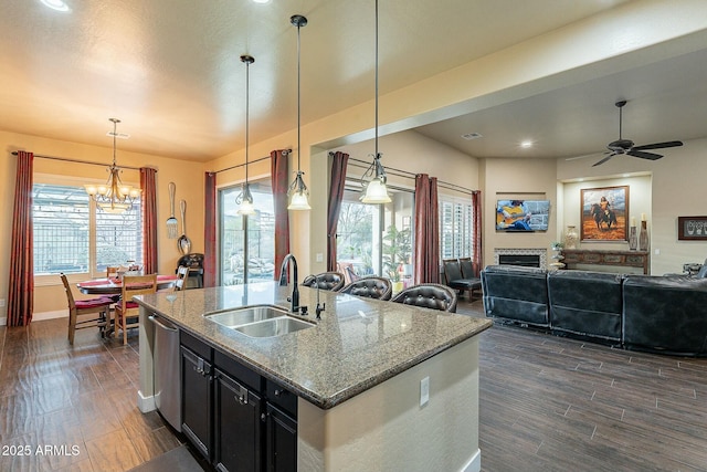 kitchen with a sink, open floor plan, dark cabinetry, light stone countertops, and dishwasher