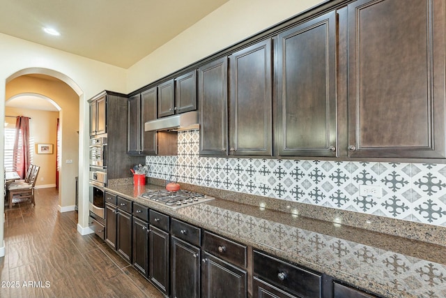 kitchen with appliances with stainless steel finishes, arched walkways, under cabinet range hood, and dark stone countertops