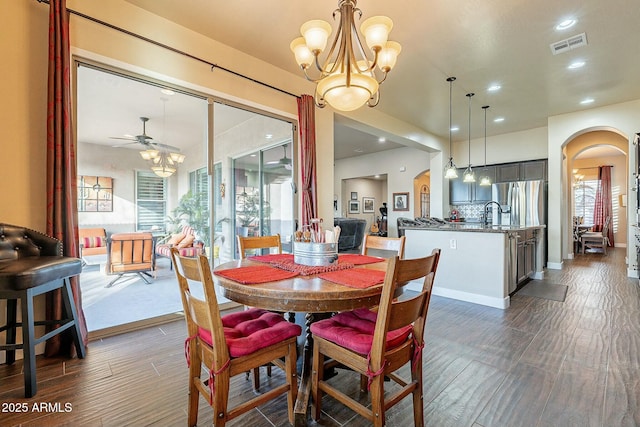 dining area featuring arched walkways, dark wood-type flooring, ceiling fan with notable chandelier, and visible vents