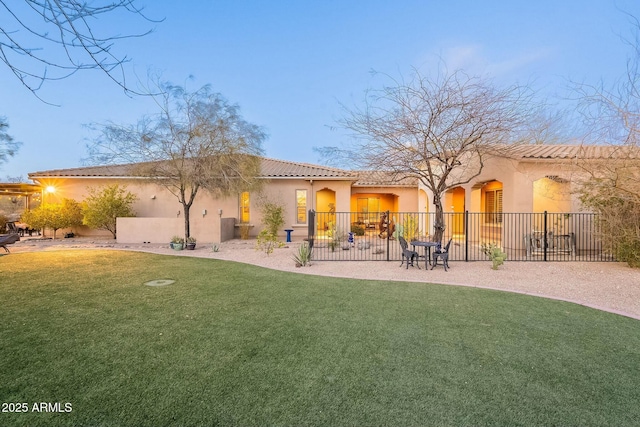 rear view of house featuring a tile roof, a yard, a patio, stucco siding, and fence