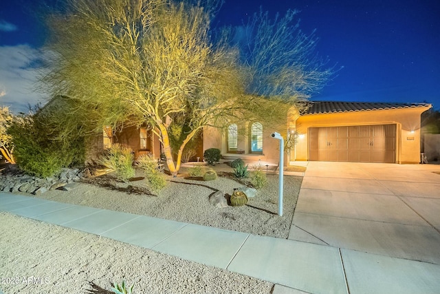 view of front of house with a garage, a tile roof, driveway, and stucco siding