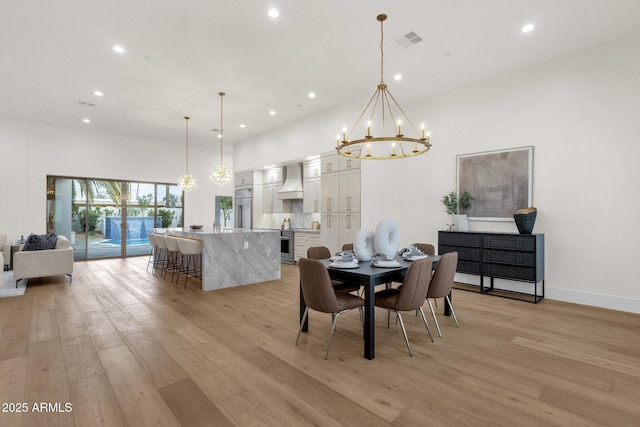 dining room featuring a high ceiling, sink, a chandelier, and light hardwood / wood-style floors