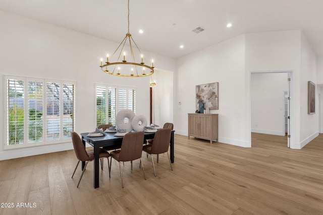 dining area with a towering ceiling, a chandelier, and light hardwood / wood-style flooring