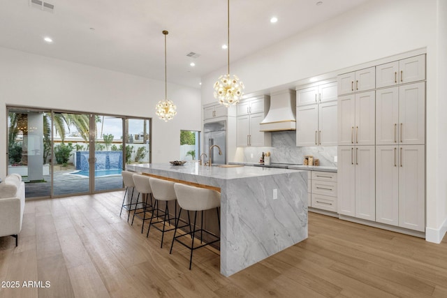 kitchen with white cabinetry, premium range hood, a center island with sink, and pendant lighting