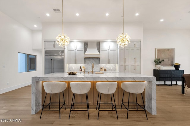 kitchen with decorative light fixtures, a kitchen breakfast bar, custom exhaust hood, stainless steel built in fridge, and a large island