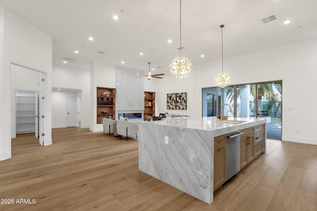 kitchen with a large island, sink, light hardwood / wood-style flooring, light stone counters, and decorative light fixtures