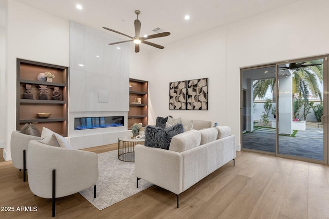 living room featuring a high ceiling, ceiling fan, a fireplace, and light hardwood / wood-style flooring