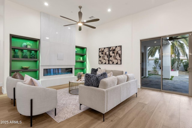 living room featuring a tiled fireplace, ceiling fan, a high ceiling, and light wood-type flooring