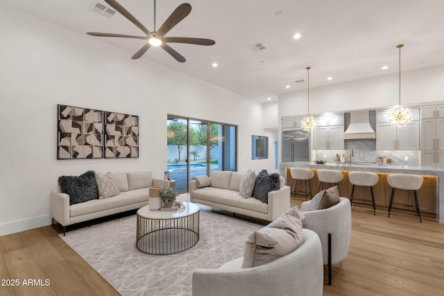 living room featuring sink, a towering ceiling, light hardwood / wood-style flooring, and ceiling fan