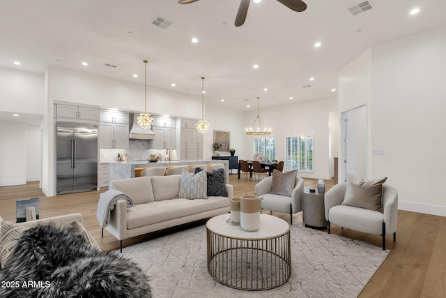 living room with sink, ceiling fan with notable chandelier, light wood-type flooring, and a towering ceiling