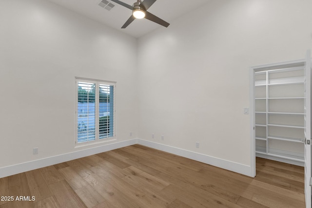 empty room with ceiling fan, light hardwood / wood-style floors, and a towering ceiling