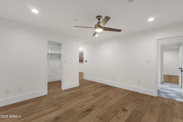 unfurnished bedroom with hardwood / wood-style floors, a walk in closet, a closet, and ceiling fan