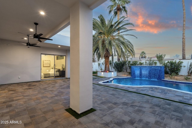 pool at dusk featuring ceiling fan and a patio