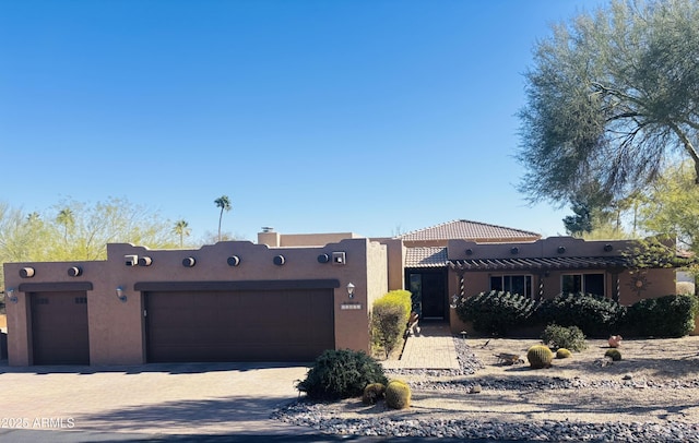 pueblo-style house featuring a garage, driveway, a tiled roof, and stucco siding