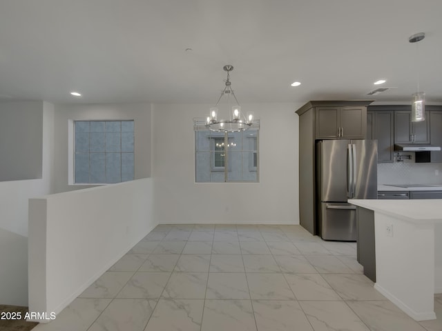 kitchen with under cabinet range hood, light countertops, recessed lighting, freestanding refrigerator, and marble finish floor