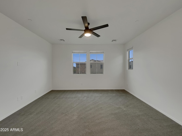 empty room featuring dark colored carpet, visible vents, baseboards, and a ceiling fan