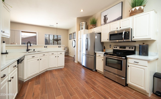 kitchen featuring sink, white cabinetry, stainless steel appliances, light stone counters, and decorative light fixtures